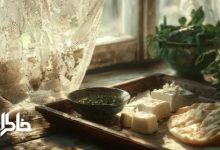 سینی چوبی با نان تازه، پنیر سفید و نعنا و سبزی خوردن کنار پنجره نورگیر با پرده‌های تور قدیمی؛ حس صبح‌های نوستالژیک ایرانی و حال‌و‌هوای مجله خاطرات.